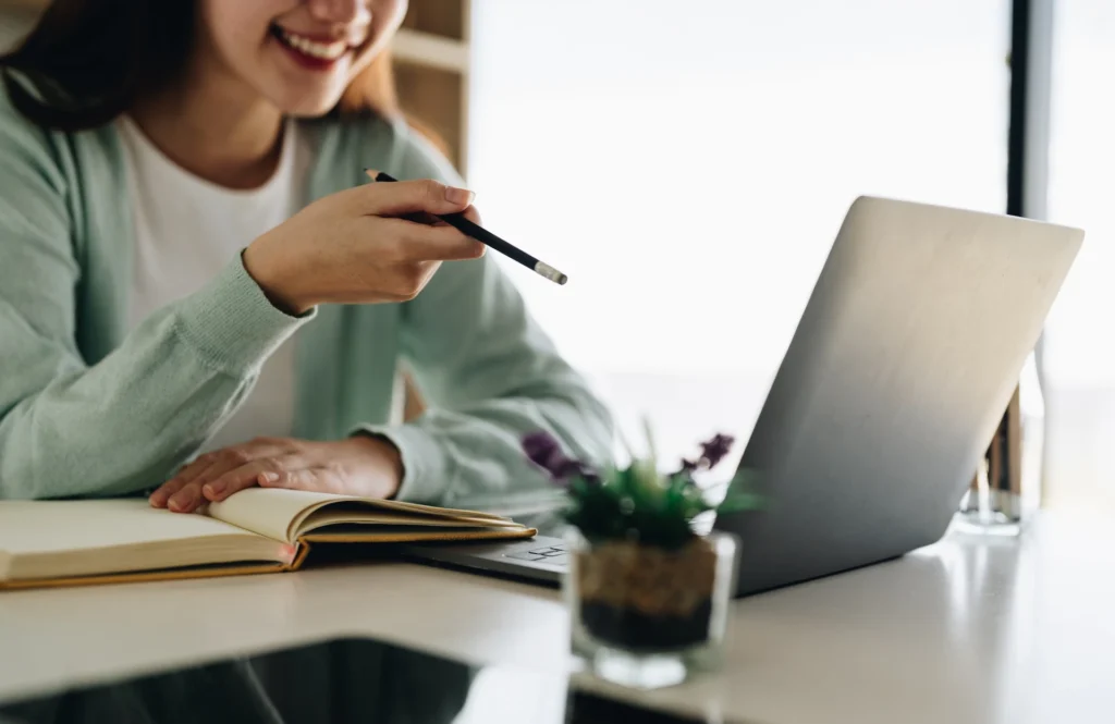 Un'immagine ravvicinata di una professionista parziale che usa un laptop e un'agenda per la formazione ESG e l'*e-learning aziendale*. La persona punta una matita verso lo schermo, a simboleggiare l'apprendimento digitale continuo per il reporting ESG e le soft skills green.
