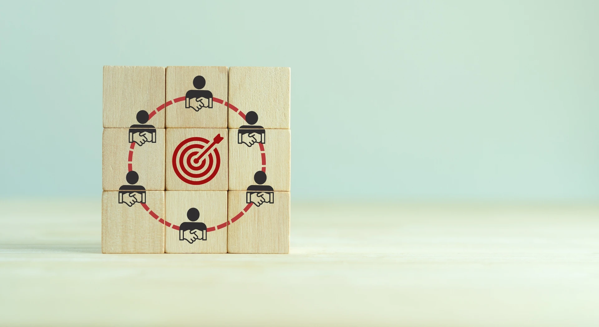 Cubi in legno con icone di persone che si stringono la mano collegate in cerchio attorno a un bersaglio rosso, a rappresentare il coinvolgimento degli stakeholder verso un obiettivo comune