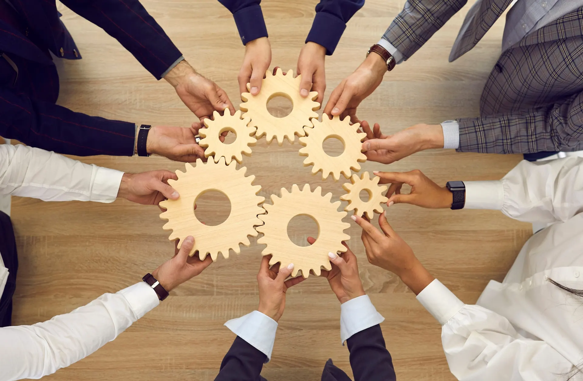 Mani di un team aziendale che uniscono ingranaggi in legno, simbolo della valutazione dell'impatto sociale d'impresa