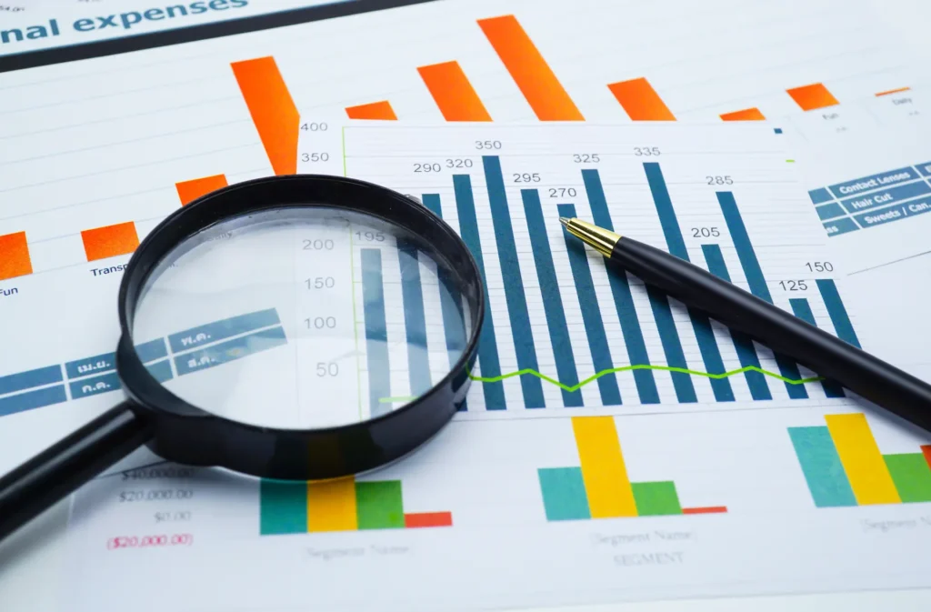 Lente d'ingrandimento e penna appoggiate su tabelle e grafici a barre stampati, a rappresentare l'analisi dei dati necessari a misurare le emissioni Scope 3