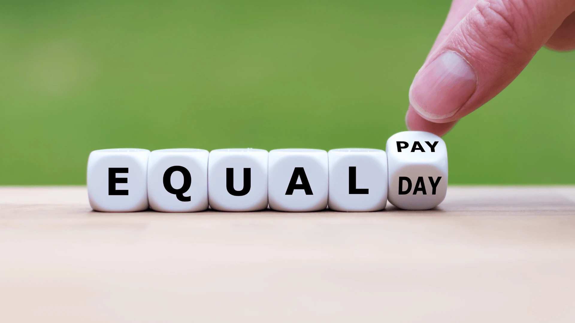 Dadi bianchi che compongono la scritta Equal Pay, con una mano che ruota l'ultimo dado